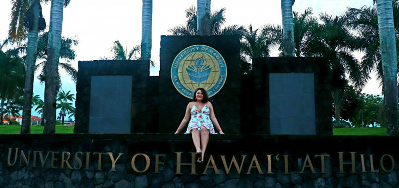 I am sitting on the wall in front of the UH Hilo sign.