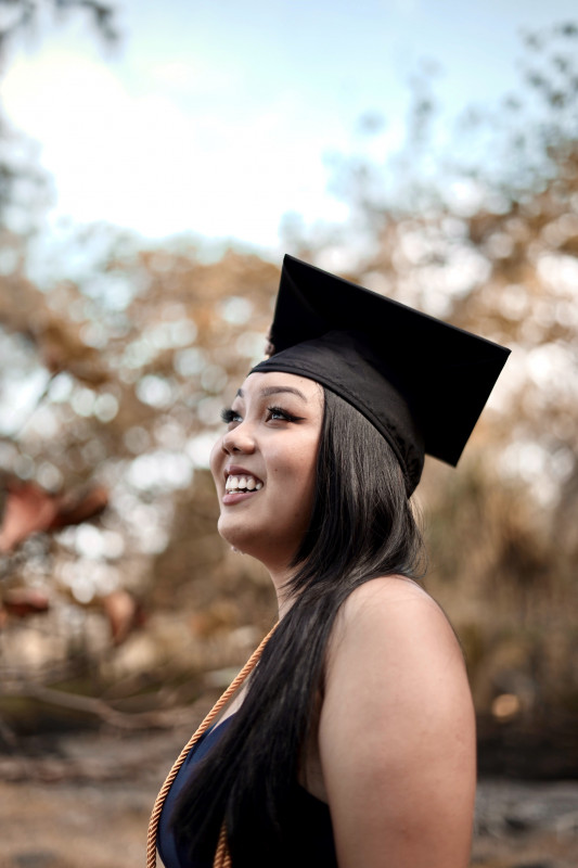 An image of me facing the ride side looking slightly up into the sky. I have my hair down over my left shoulder on the front. I am wearing my cap with my blue dress and gold cord on my shoulders.