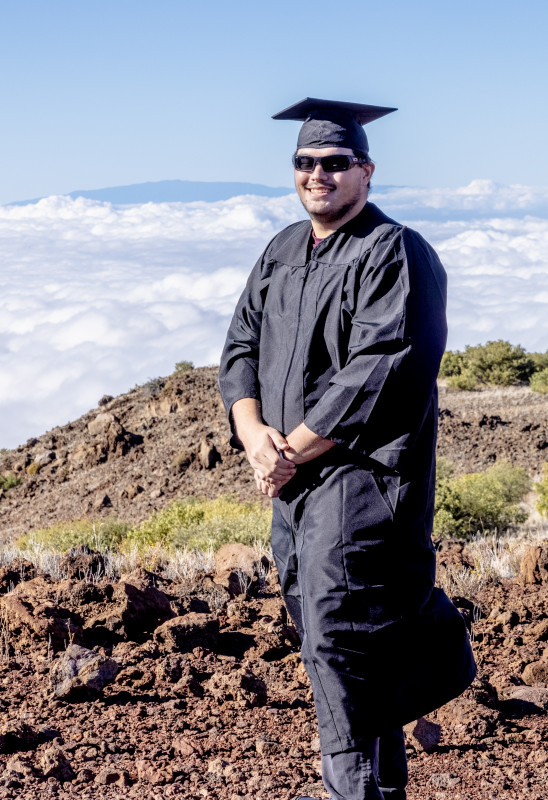 This picture is of me wearing my cap and gown on top of the rocky environment of Mauna Kea. I am high in elevation so the clouds in the background are lower and Hualālai (another mountain of the Big Island) is also seen peaking above the clouds.