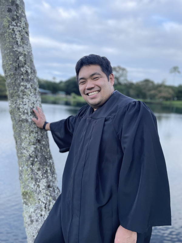 Andrew standing a next to a tree. He is very excited to graduate.