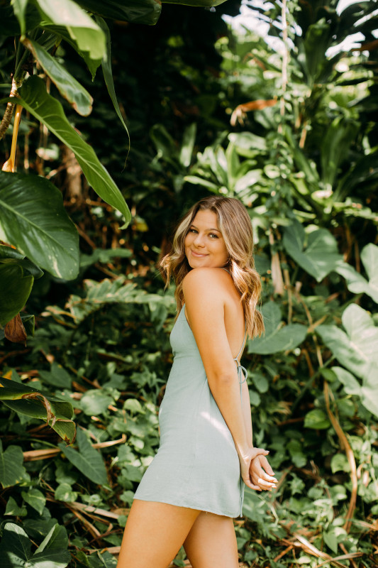 Photo was taken at Honoli'i Beach Park with the green leaves in the background. Shae is wearing a sage color dress and hair curled looking over her shoulder smiling