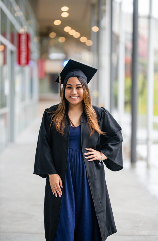 Smiling with hand on hip in a black cap and gown