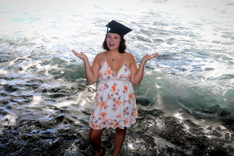 I am standing in the ocean, wearing a white flowered dress and my graduation cap. I am smiling and holding my hands up.  I would like for this to be my primary picture.