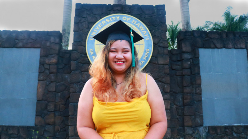 mid-laugh with my graduation cap in front of the school logo