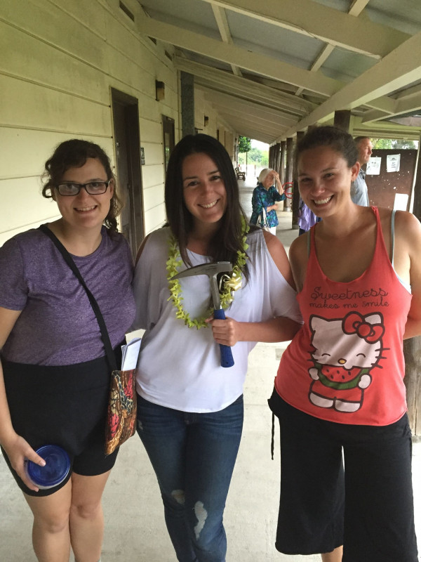 Michelle Mazzetti standing in front of the Geology Department holding a Rock Hammer and with a green orchid Lei.