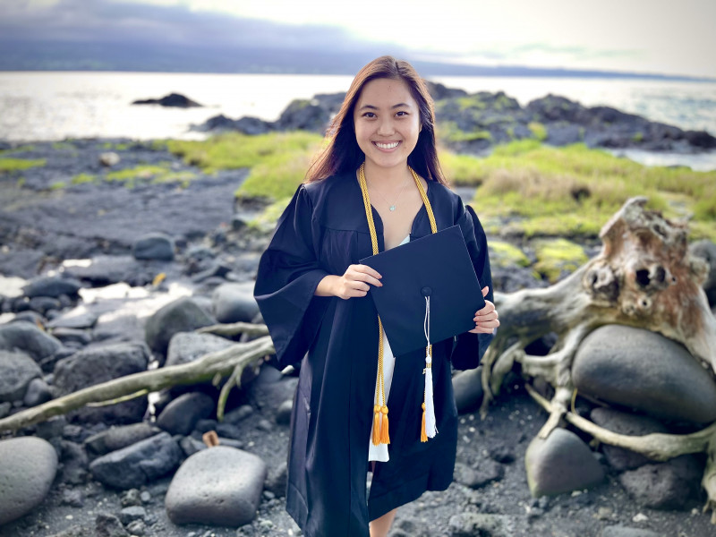 Taylor holding graduation cap. Background is a black sand beach.