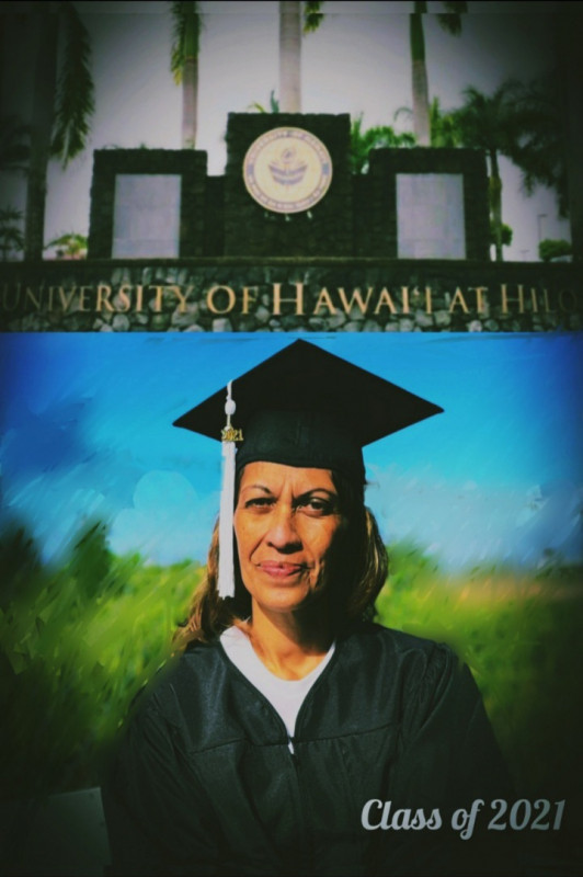Upper body shot of graduate in cap and gown with blue sky and green grass, both blurred, in the background. Attached above is the UH Hilo sign on stoned wall.