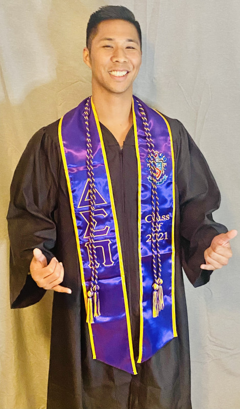 Graduate wearing commencement gown and honors society stole and cords give shakas.