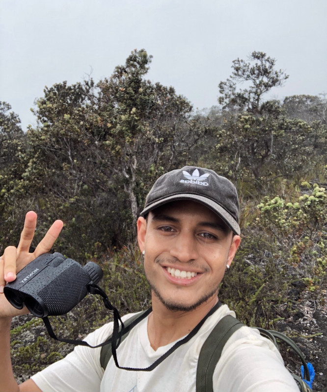 Kūpono holding binoculars in the forest