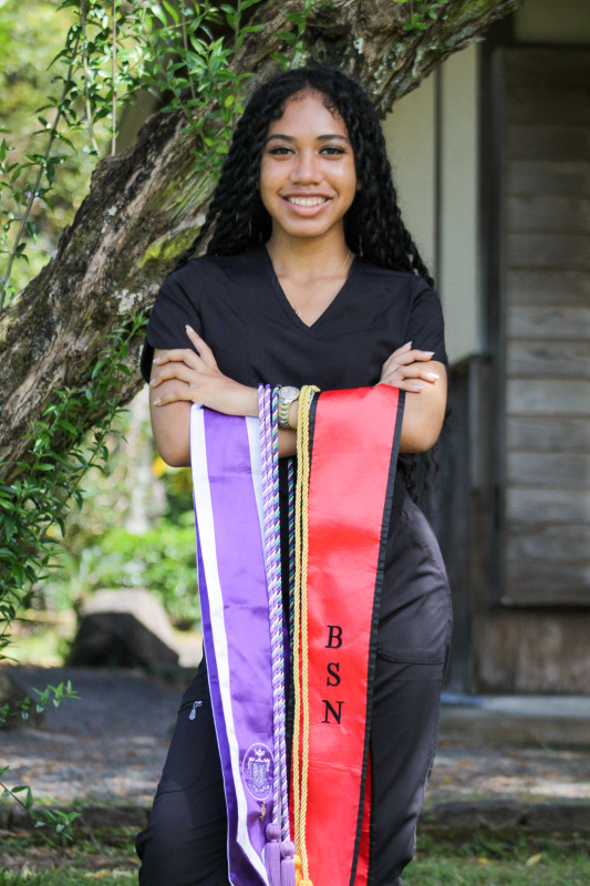 Graduate in black scrubs holding 2 stoles and 3 cords
