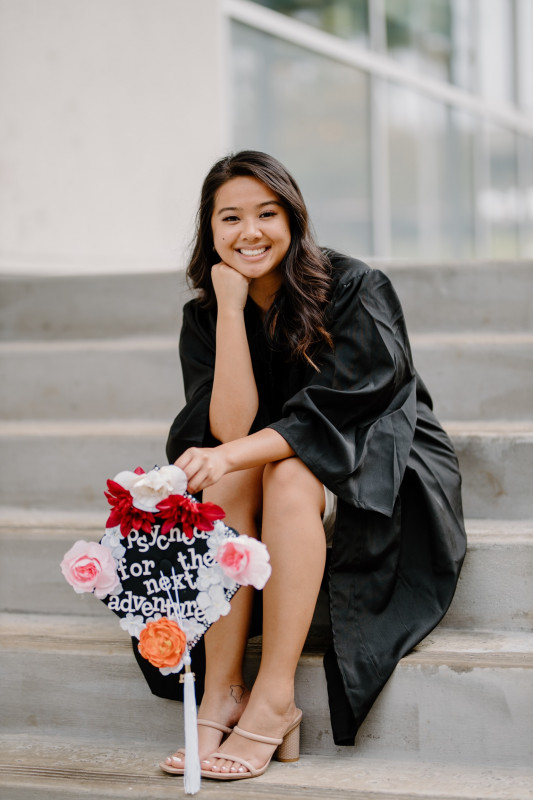 Sitting down with in my graduation gown and holding my cap.