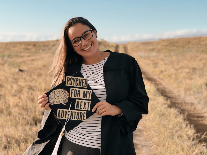 Myself smiling at the camera holding my graduation cap which states "psyched for my next adventure"