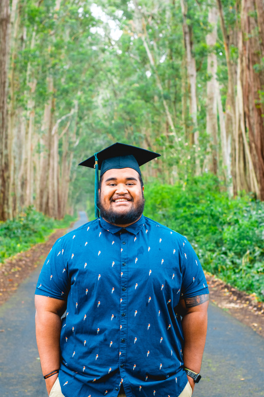 Standing amidst tall trees dressed formally in a blue button-up and wearing my cap with the tassel.