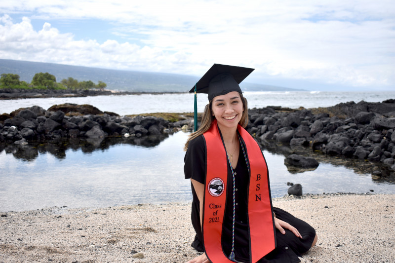 Lexie sitting on a beach, wearing cap and gown