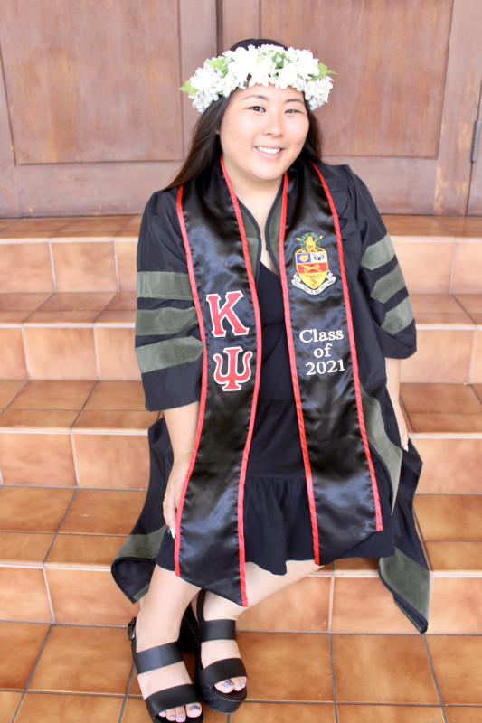 Brooke is sitting on a staircase wearing her doctoral regalia