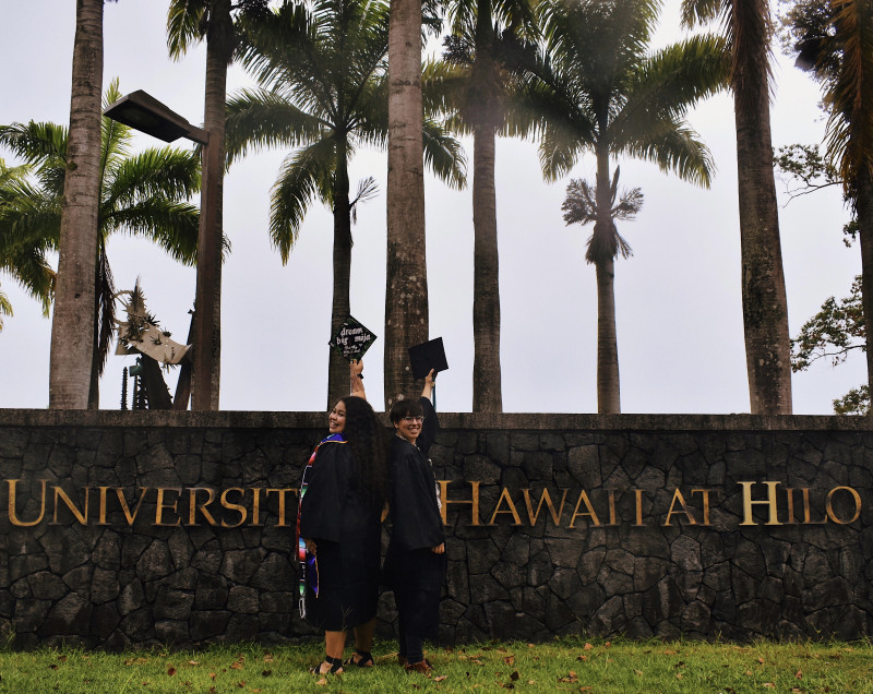 Graduates standing in front of the UH Hilo Sign with their caps in the air