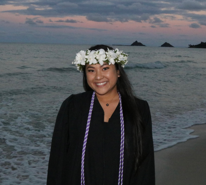 Courtney Malina wearing a haku and graduation gown at sunset.