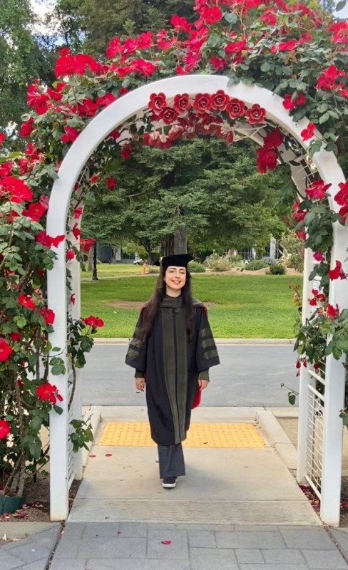 This is a picture of Michelle in her graduation cap and gown, walking through an arched trellis.
