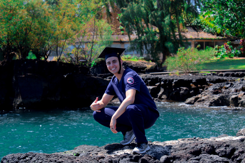 Squatting in a graduation cap and scrubs looking good