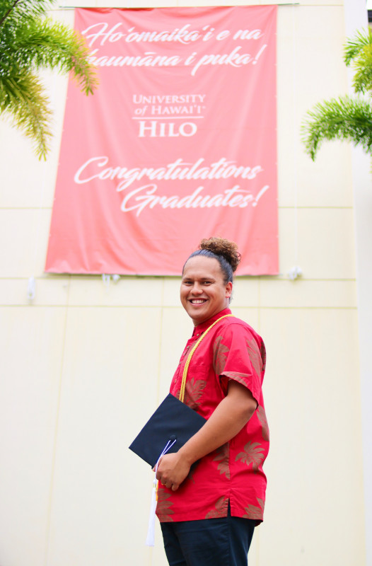My third photo is of me standing outside in front of the red banner congratulating graduates. My hair is up with my cap in my left hand.