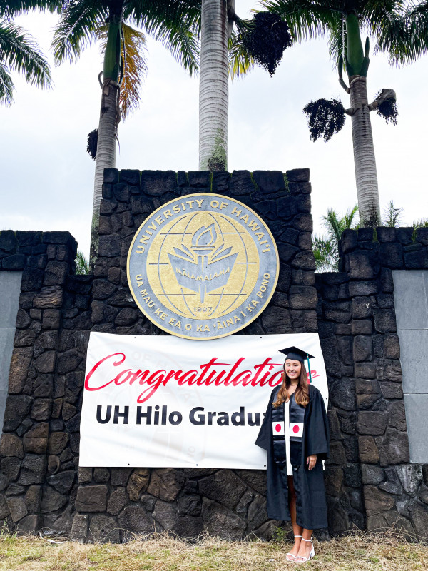 I'm standing in front of the UHH rock wall sign with cap and gown