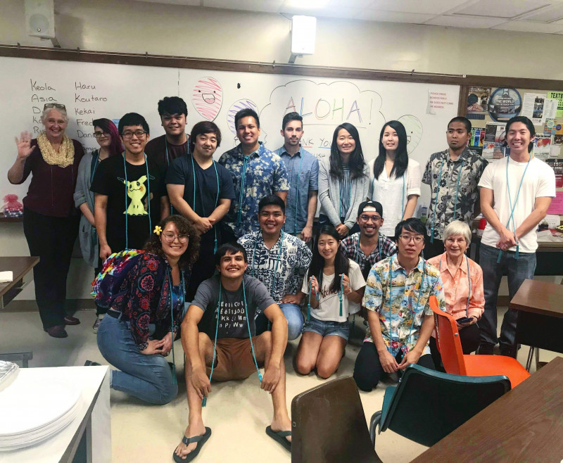 17 of the TESOL program graduates are smiling with the program coordinator, Bela, who is standing on the far left. It was a potluck, so some plates are visible on the bottom right. Many of us are wearing aloha shirts and dressed nicely for the event. It was the last teaching week of the program, so we decided to throw a party after our free English lessons.