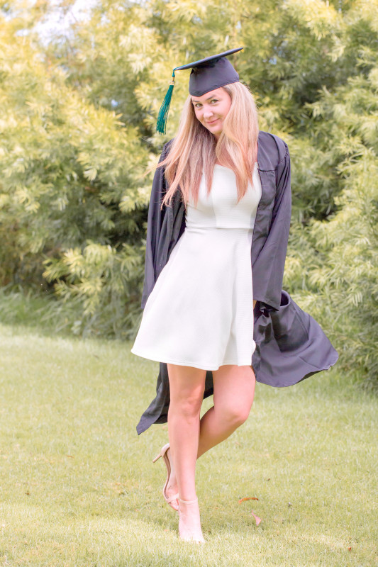 Michelle Mazzetti wearing her Cap and Gown standing in front of a green hedge.