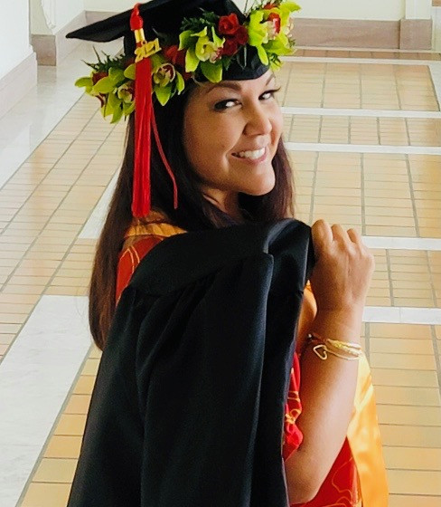 holding black gown with cap and haku  lei with red 2021 tassel