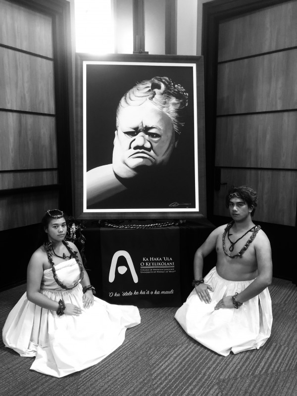 wahine and kane posing seriously with a painting of Ruth Keʻelikōlani.