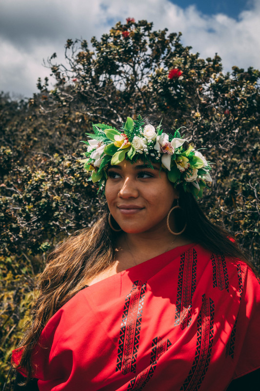 Wahine Wearing red kihei and grinning and looking into the distance.