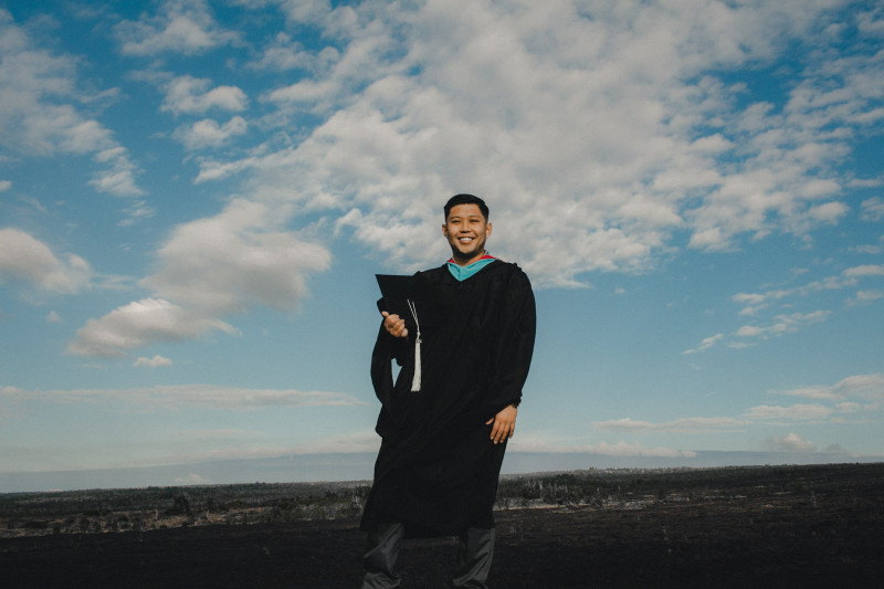 Dressed in master's regalia with cap in hand.