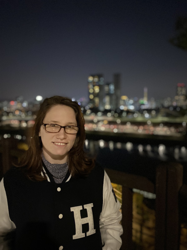 Sienna Wareham standing in a letterman jacket with the Han river behind her