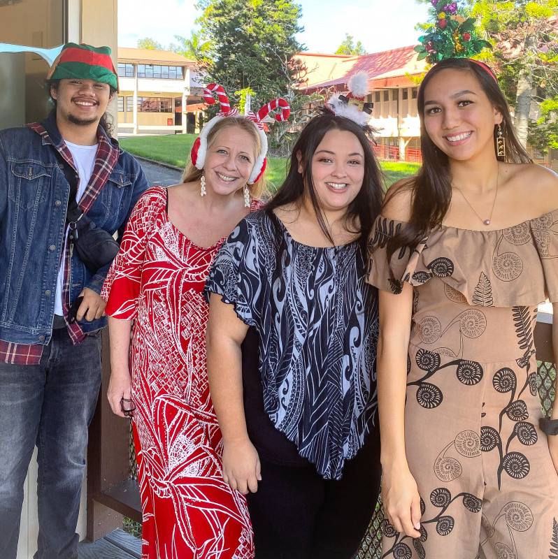 Picture of UH Hilo Testing Center staff (there are four of us, I am second from the left) wearing aloha theme attire and Christmas head wear. Picture taken in front of UH Testing Center, in the background shows partial of K-Building and HCC Bus. Ed. and Tech.