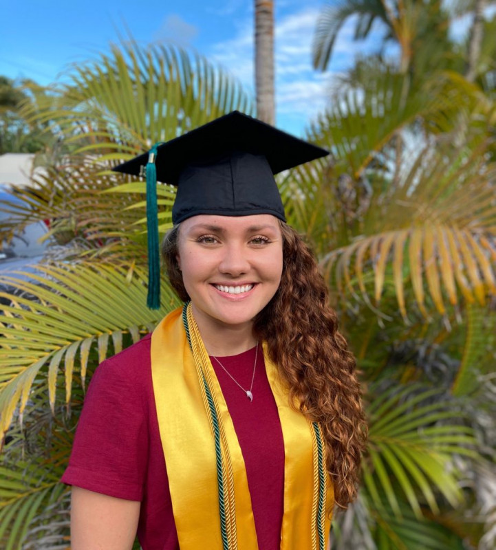 Graduate with cap in-front of foliage smiling