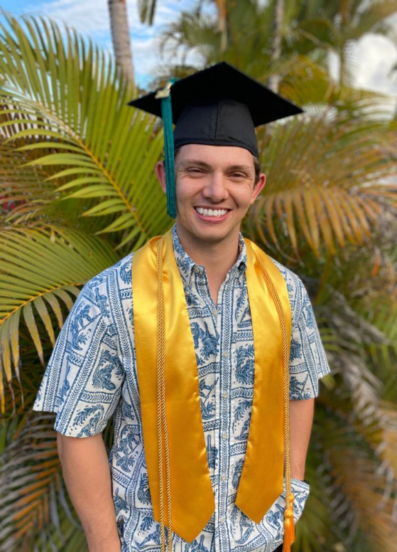 Graduate with cap in-front of plants smiling