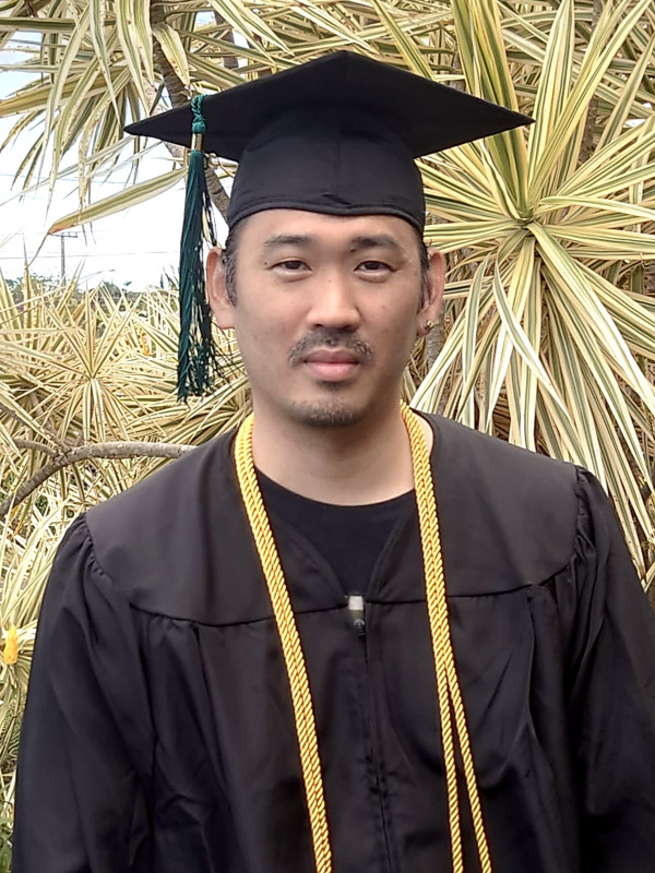 John in his cap and gown in front of a yellow dracaena sunshine plant