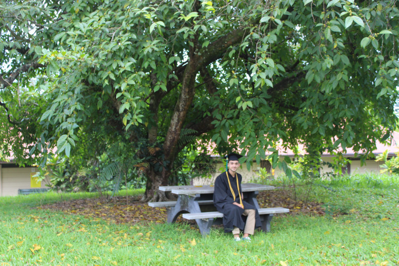 Max sitting on a bench on campus in his cap and gown.