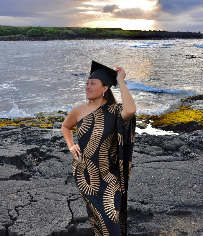 Malie Ibarra wearing a gold and black dress and a graduation cap at the beach