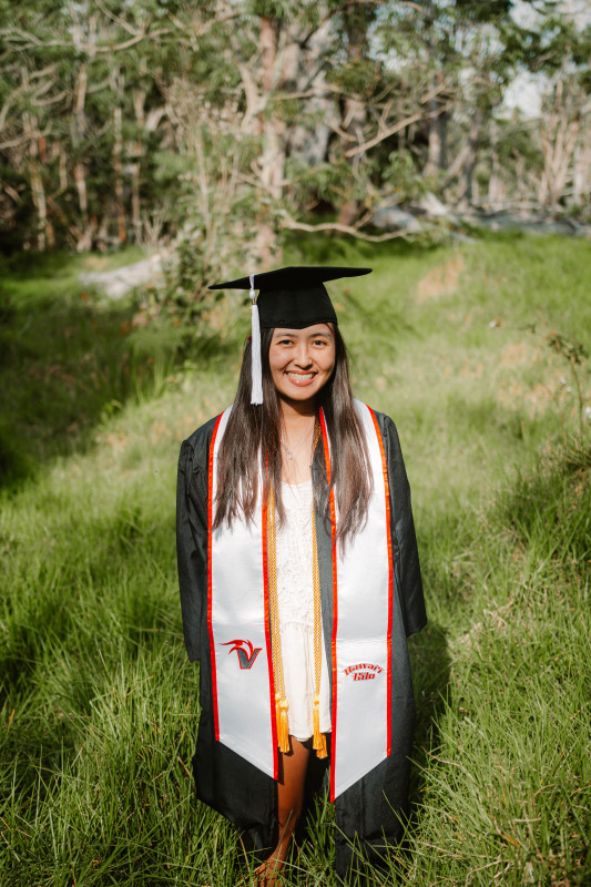 Me standing in a field of grass with my cap and gown, honor cord, and Vulcan sash.
