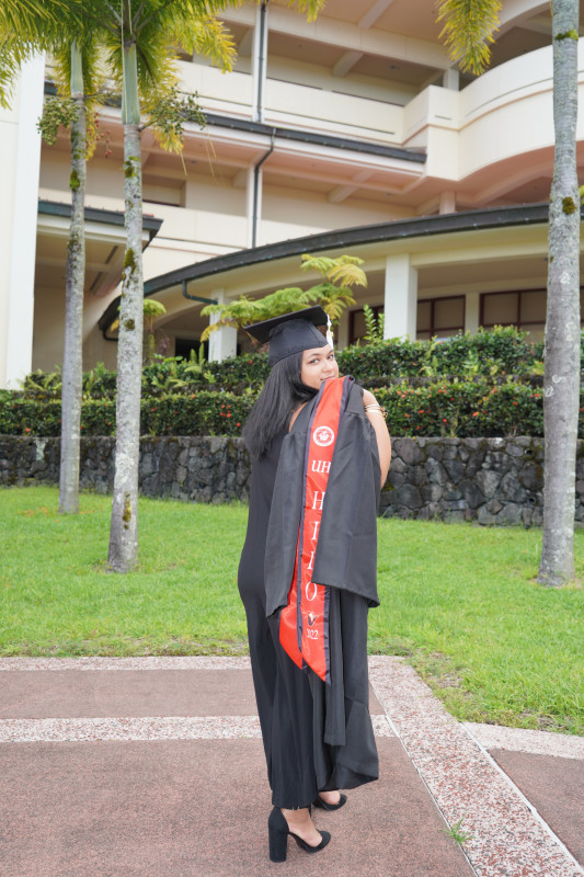 Graduate, standing in front of the school of education building also known as UCB in her cap with her gown placed behind her shoulder