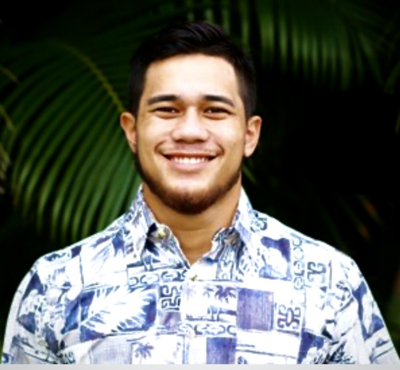 A smiling headshot with palm leaves in the background.I have a white aloha shirt on with my hair slicked to the side as a comb over.