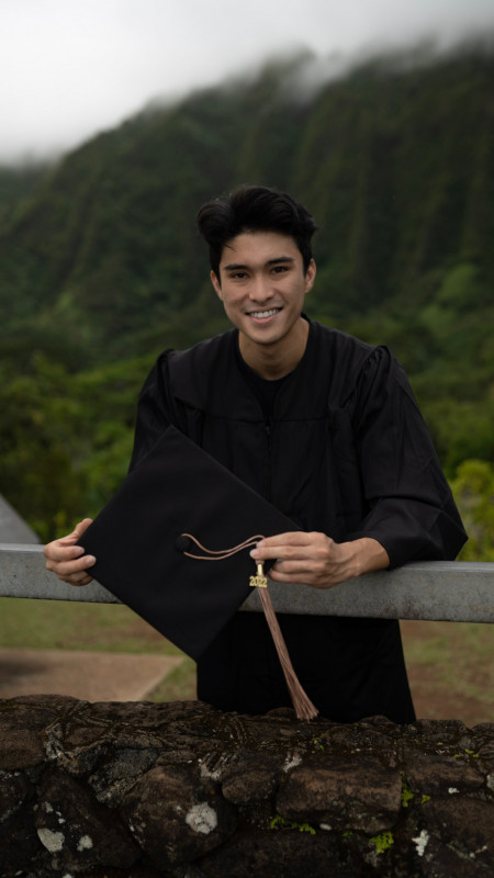 Graduation picture with gown on while leaning on railing in front of me