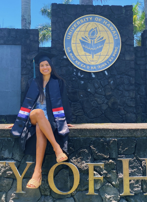 Sofia with her cap and gown in front of the UHH sign
