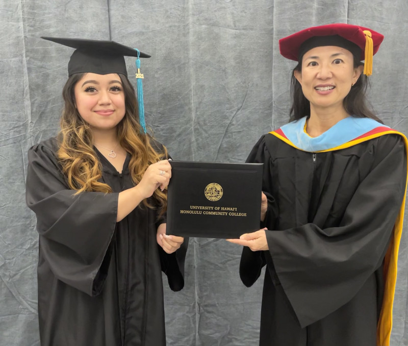 I am holding my diploma from one end and the chancellor, Karen Lee, is holding the other end. We are both smiling facing the camera.