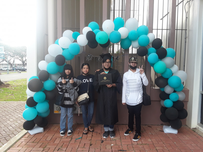 Me standing next to my mother, my brother and my sister under a balloon arch, colored teal, black and white