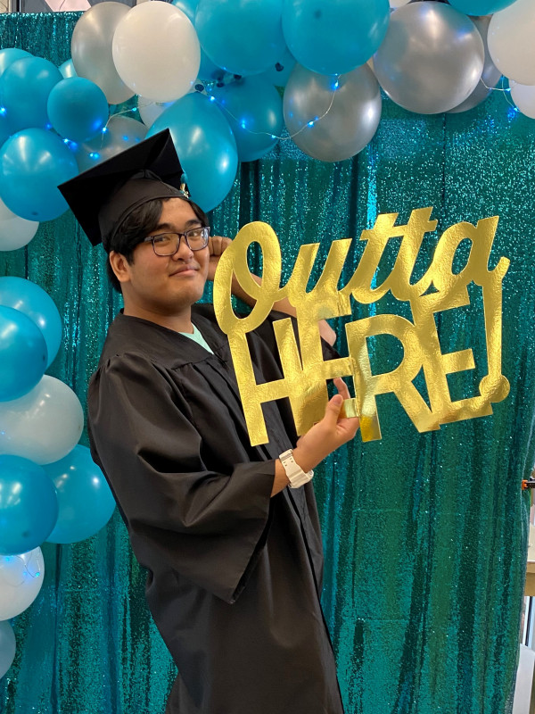 Hitchhiking with my thumbs up in cap and gown, holding a sign saying "Outta Here"