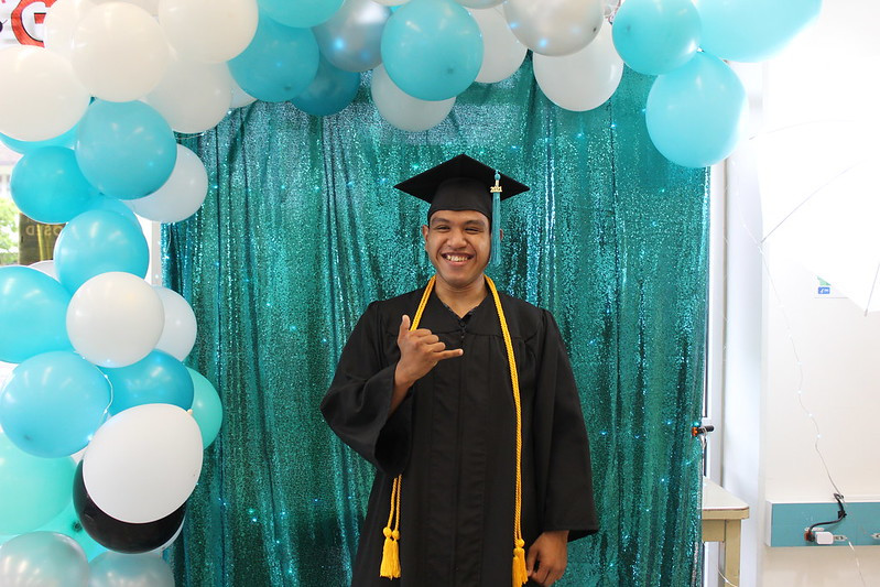 this is me wearing my cap and gown as I pose with a Shaka towards the camera