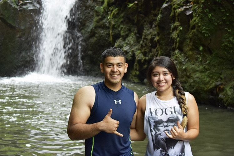 It’s a picture of my partner and I hugging, while doing the Shaka sign. There’s a waterfall on the background.