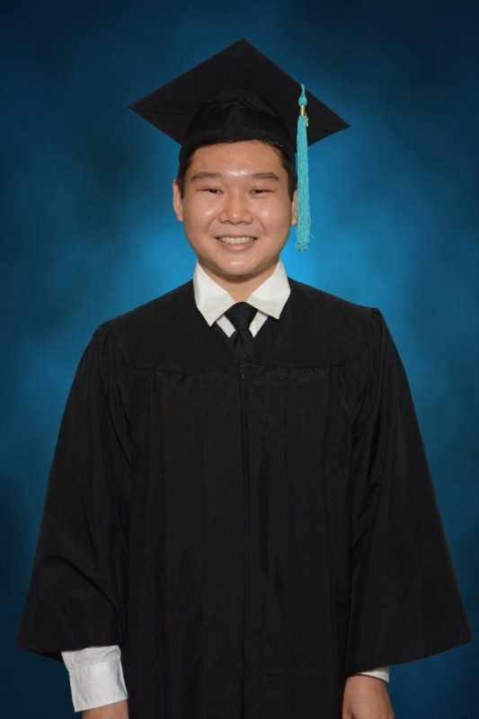 There is a dark blue background and I'm wearing a black cap and gown with a teal tassel.