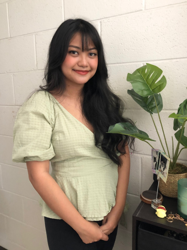 Photo of myself in a green blouse, standing next to a plant.